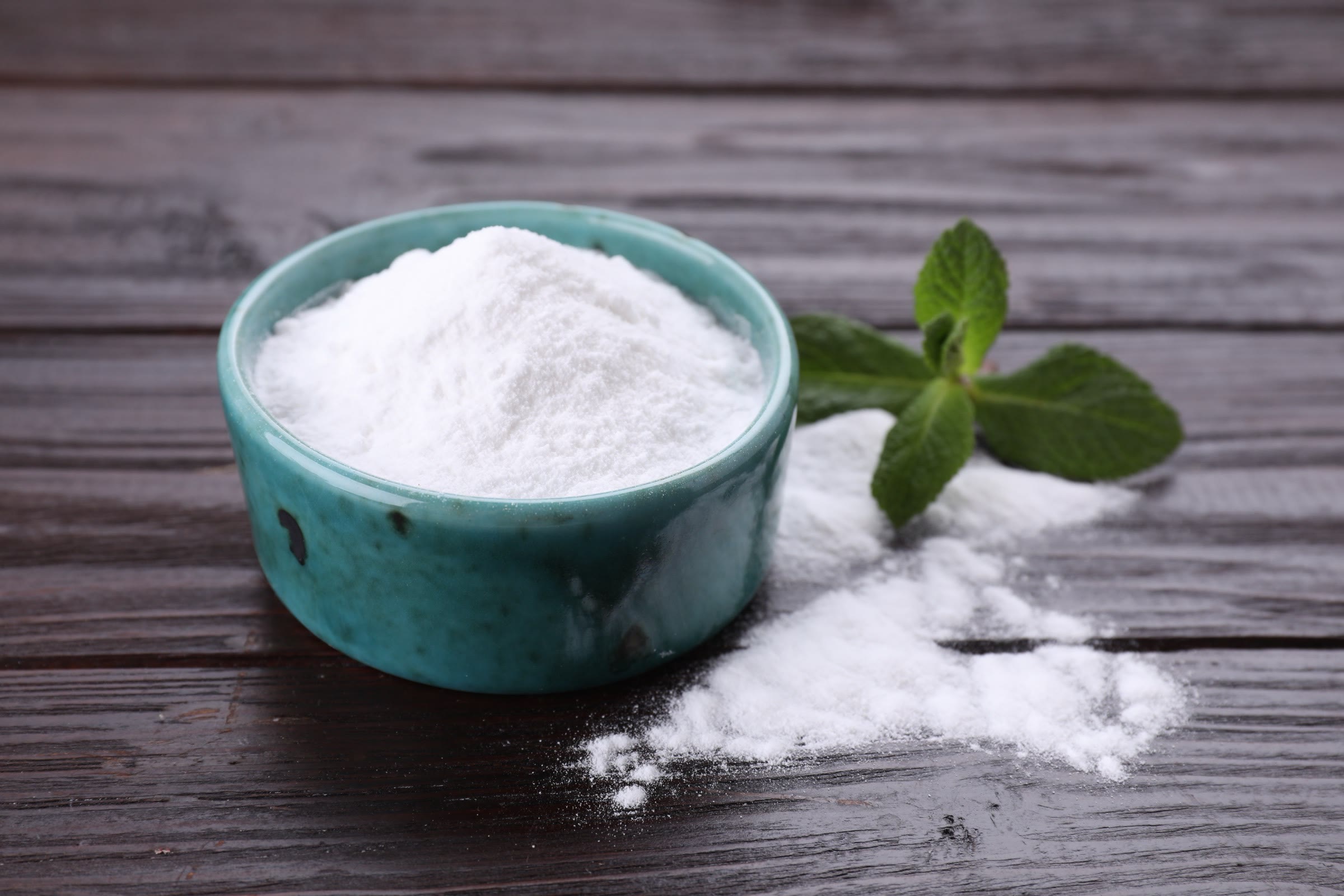 Pale powder in a small bowl with a fresh mint sprig on dark wood
